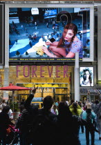 USA, New York, Manhattan, People waving and looking at themselves in a giant live real time TV video LED screen in Times Square above Forever 21 clothing shop.