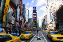 USA, New York, Manhattan, People walking in Times Square at the junction of 7th Avenue and Broadway below buildings with advertising on large video screens with yellow taxi cabs driving down 7th Avenu...