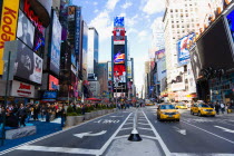 USA, New York, Manhattan, People walking in Times Square at the junction of 7th Avenue and Broadway below buildings with advertising on large video screens with yellow taxi cabs driving down 7th Avenu...