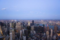 USA, New York, Manhattan, View from Empire State building over midtown skyscrapers and East River towards Queens and Long Island with Art Deco Chrysler Building illuminated at sunset.