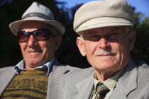 Albania, Tirane, Tirana, Head and shoulders portrait of two men. One elderly looking straight to camera, one wearing sun-glasses slightly behind, both wearing hats.