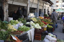 Albania, Tirane, Tirana, Customer and vendors at fruit and vegetable stalls in the Avni Rustemi market with display including carrots, lettuce, aubergines, peppers and oranges.