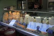 Albania, Tirane, Tirana, Cheese shop in the Avni Rustemi Market with young male vendor behind counter display.