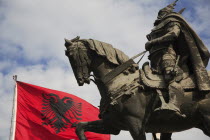 Albania, Tirane, Tirana, Skanderbeg Square, Part view of equestrian statue of national hero George Castriot Skanderbeg also known as The Dragon of Albania beside red flag with double headed eagle embl...