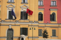 Albania, Tirane, Tirana, Part view of pink and yellow exterior facade of government buildings in Skanderbeg Square flying flags including double headed eagle emblem. Multiple windows with green painte...