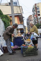 Albania, Tirane, Tirana, A street vendor using hand held set of scales to weigh fruit for elderly woman customer carrying bags.