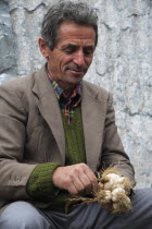 Albania, Tirane, Tirana, Portrait of a male street vendor bunching bulbs of garlic together for sale.
