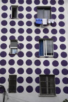 Albania, Tirane, Tirana, Part view of exterior facade of apartment block painted with pattern of purple coloured circles. Windows with washing hanging from uppermost.