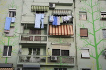 Albania, Tirane, Tirana, Detail of exterior facade of apartment block painted with tree forms in green and yellow with washing hanging from balconies and window ledge.