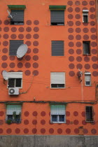 Albania, Tirane, Tirana, Detail of exterior facade of apartment block painted orange with pattern of red circles, multiple windows and satelite dishes.