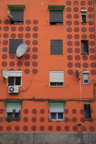 Albania, Tirane, Tirana, Detail of exterior facade of apartment block painted orange with pattern of red circles, multiple windows and satelite dishes.