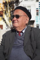 Albania, Tirane, Tirana, Head and shoulders portrait of an elderly man wearing beret and sunglasses. Three-quarter profile left.