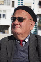 Albania, Tirane, Tirana, Head and shoulders portrait of an elderly man wearing sunglasses and a beret. Three-quarter profile left.