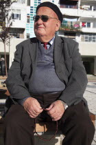 Albania, Tirane, Tirana, Three-quarter portrait of an elderly man wearing black beret and sunglasses, seated, turned to left, and holding prayer beads.