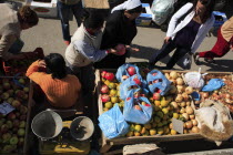 Albania, Tirane, Tirana, Looking down on stall of street vendor selling apples, pomegranates and onions sitting beside set of scales with female customers making purchases.