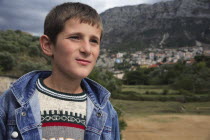 Albania, Kruja, Head and shoulders portrait of a teenage boy with the town of Kruja in the background.