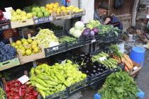 Albania, Tirane, Tirana, Display of fruit and vegetables including peppers, cabbage and grapes at grocers shop in the Avni Rustemi market. Shoe mender in doorway at side.  