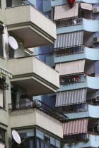 Albania, Tirane, Tirana, Detail of balconies, striped awnings and satellite dishes on blue painted exterior facade of apartment block.
