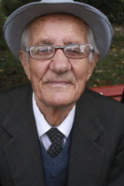 Albania, Berat, Head and shoulders portrait of an elderly man wearing hat and glasses, looking straight to camera.