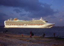 England, Hampshire, Southampton Water, The cruise ship Azura passing Calshot Spit on her maiden voyage to the Mediterranean. People watching from pebble beach in foreground.