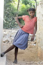 Haiti, La Gonave Island, Young happy smiling girl leant against the wall of a slum building.