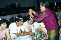 Thailand, Bangkok, Couple being symbolically bound together with cotton during Thai Buddhist wedding ceremony.