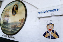 ENGLAND, Hampshire, Portsmouth, Wall paintings outside a tattooist's parlour underneath railway arches at Portsmouth Harbour Station showing a sailor with the local football club slogan Play Up Pomley...