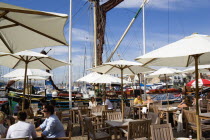 England, Hampshire, Portsmouth, Port Solent People at restaurant tables under sun shade umbrellas with yachts moored in the marina and housing beyond.