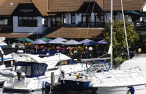 England, Hampshire, Portsmouth, Port Solent Boats moored in the marina with people sitting at restaurant tables beyond.