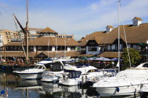 England, Hampshire, Portsmouth, Port Solent Boats moored in the marina with people sitting at restaurant tables beyond beside a pub and housing apartments.