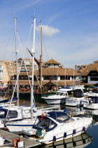 England, Hampshire, Portsmouth, Port Solent Boats moored in the marina with people sitting at restaurant tables beyond beside a pub and housing apartments.