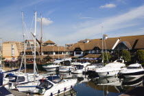 England, Hampshire, Portsmouth, Port Solent Boats moored in the marina with people sitting at restaurant tables beyond beside a pub and housing apartments.