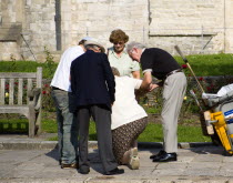 ENGLAND, Hampshire, Portsmouth, People helping an elderly lady to stand up after she has fallen on the pavement sidewalk outside the Anglican Cathedral in Old Portsmouth.