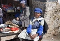 China, Yuunan, Baisha, Old Naxi woman wearing traditional costume, selling goods on market stall in the village near Lijiang.