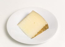 Food, Dairy Product, Cheeses, Slice of Spanish Manchego cheese made from pasteurised Manchega sheep's milk from the La Mancha region of Spain on a round white plate against a white background.