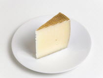 Food, Dairy Product, Cheeses, Slice of Spanish Manchego cheese made from pasteurised Manchega sheep's milk from the La Mancha region of Spain on a round white plate against a white background.