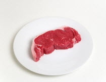 Food, Red Meat, Beef, Slice of raw uncooked sirloin steak on a round white plate against a white background.