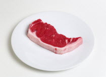 Food, Red Meat, Beef, Slice of raw uncooked sirloin steak on a round white plate against a white background.