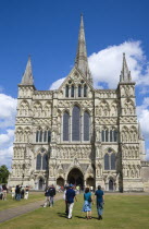 England, Wiltshire, Salisbury, People on the grass of the Close in front of the West Front main entrance of the 13th Century Early English Gothic Cathedral Church of the Blessed Virgin Mary with the t...