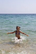 Greece, Macedonia, Halkidiki, Toroni, Young smilling girl playing at the sea throwing water and laughing.