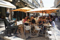 Portugal, Lisbon, Cafe a Brasileira with people sat outside next to the statue of poet Fernando Pessoa.