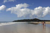 Australia, New South Wales, Byron Bay, tourists walking along the sandy shore.