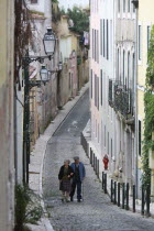 Portugal, Lisbon, Elderly couple walking along a cobbled street in the Bairro Alto district.
