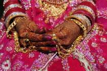 India, Uttarakhand, Hardiwar, cropped shot of hands of a woman held in lap and decorated with henna, wearing pink beaded sari, gold jewellery and multiple bracelets.