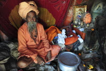 India, Uttarakhand, Hardiwar, Portrait of Saddhu sitting inside makeshift tent surrounded by belongings during Kumbh Mela,  Indias biggest religious festival where many different traditions of Hinduis...