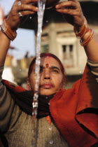 India, Uttarakhand, Hardiwar, Woman pilgrim with arms raised to pour Ganges water from vessel during Kumbh Mela, Indias biggest religious festival where many different traditions of Hinduism come together to bathe in the Ganges.