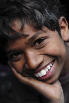 India, Uttarakhand, Hardiwar, Close cropped portrait of smiling young boy with head resting on his hand.