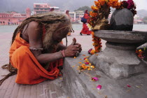 India, Uttarakhand, Hardiwar, Saddhu praying at shrine draped with flower garland offerings during Kumbh Mela, Indias biggest religious festival where many different traditions of Hinduism come togeth...