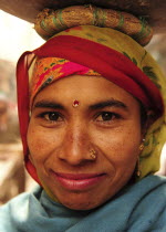 India, Uttarakhand, Hardiwar, Head and shoulders portrait of smiling young woman carrying vessel on her head.