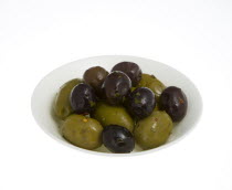 Food, Fruit, Olives, Ripe black and green olives Olea europaea in olive oil in a bowl against a white background.